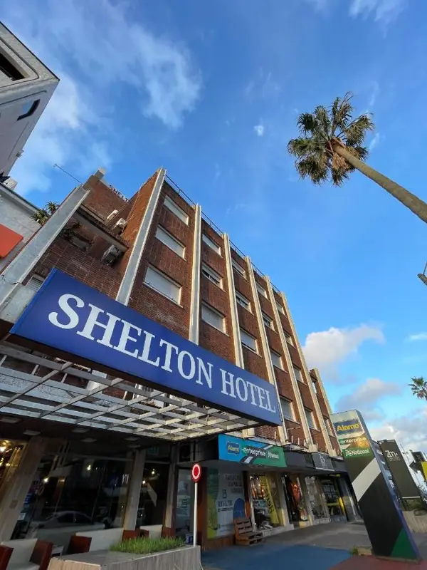 Fachada del Hotel Shelton en Punta del Este, con el cartel azul y una palmera